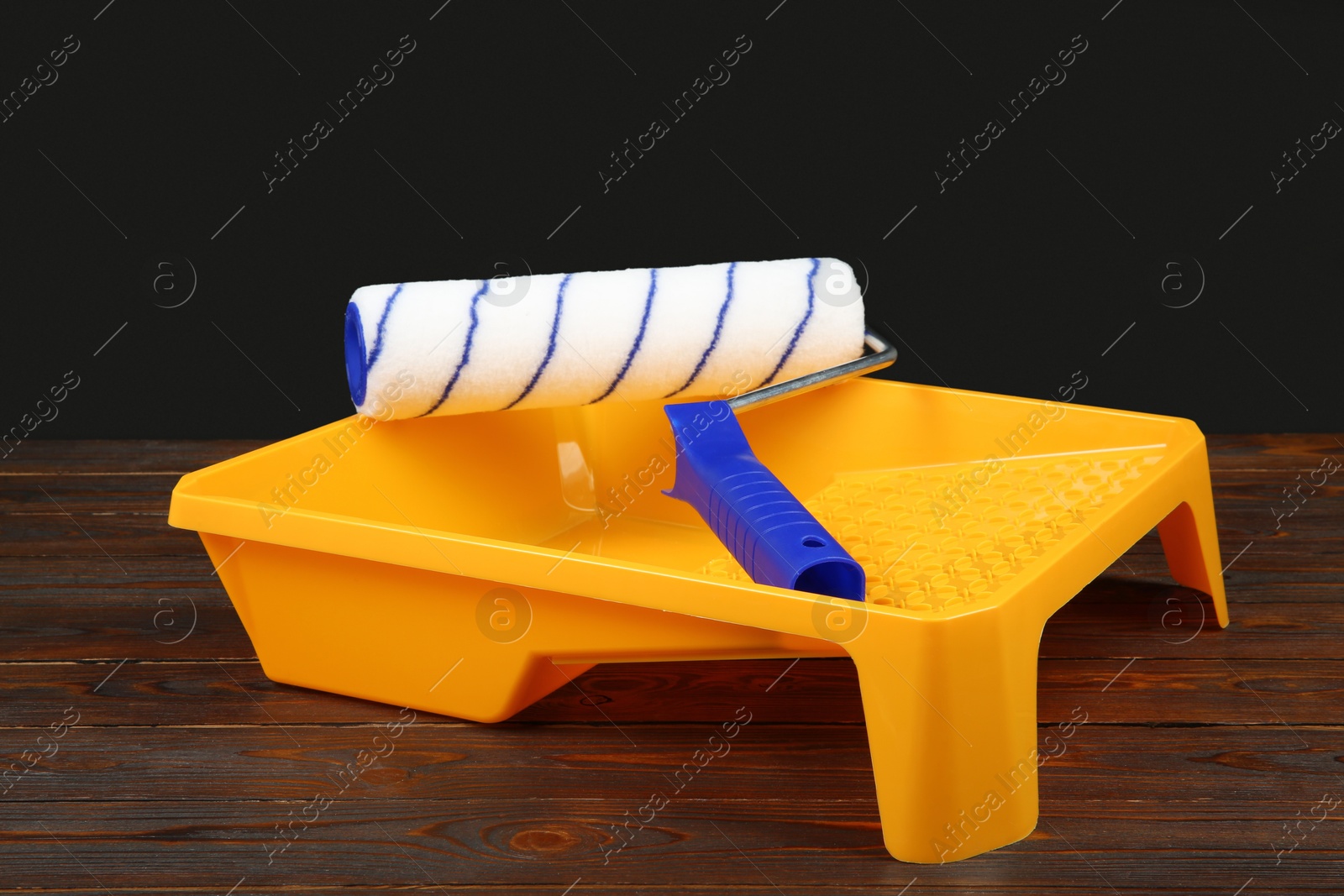 Photo of Tray and paint roller on wooden table. Construction tools