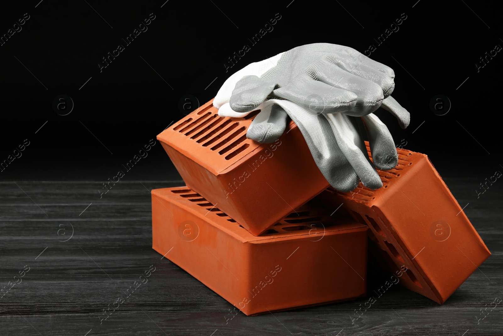 Photo of Red bricks and rubber gloves on wooden table. Building material