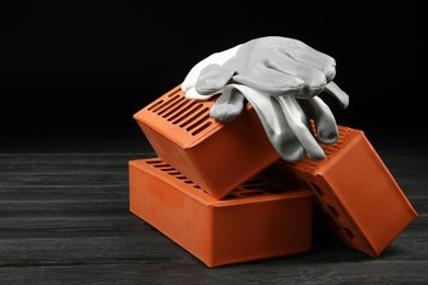 Photo of Red bricks and rubber gloves on wooden table. Building material