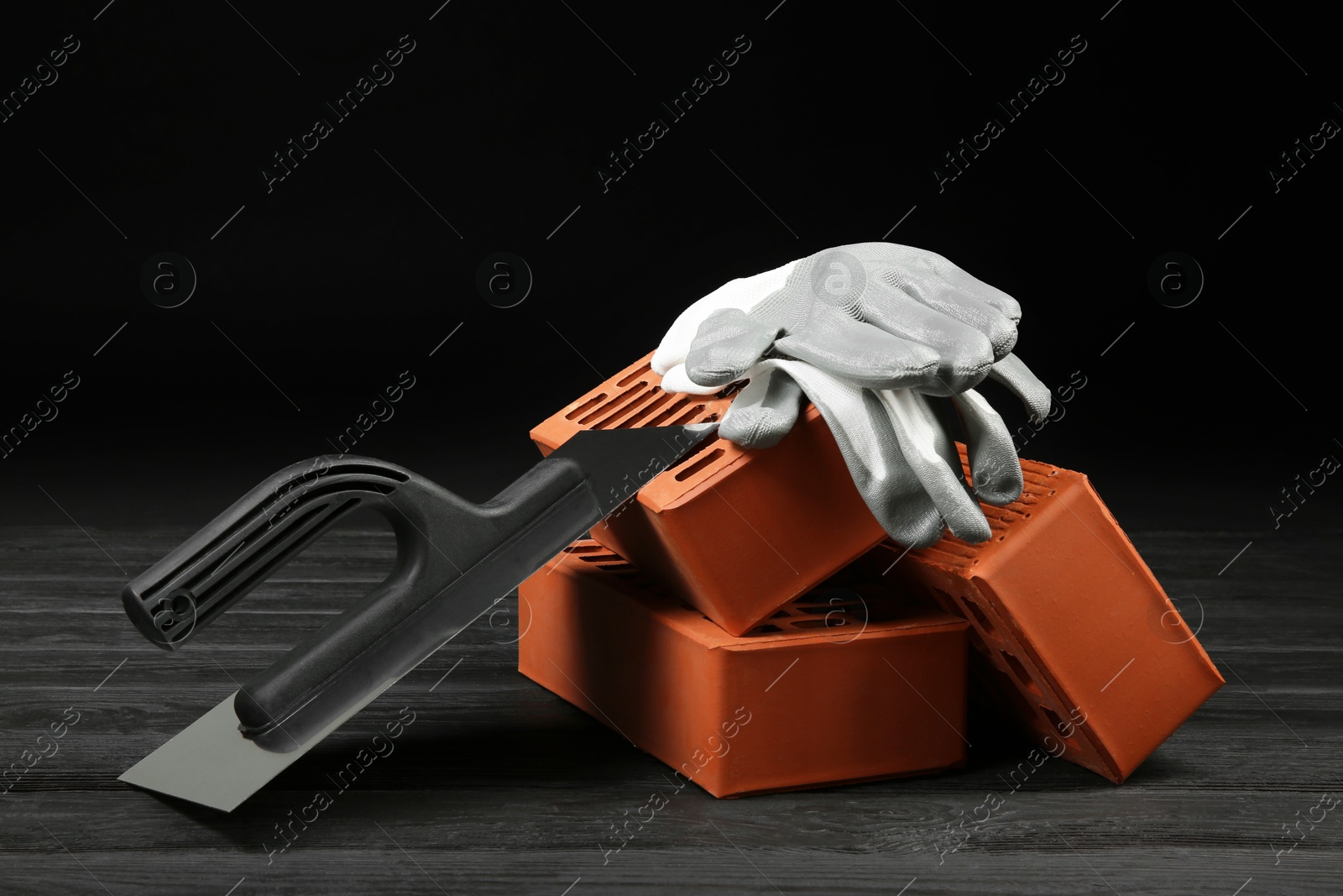 Photo of Red bricks, putty knife and rubber gloves on wooden table. Building material