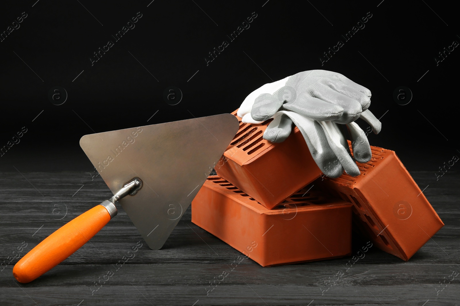 Photo of Red bricks, putty knife and rubber gloves on wooden table. Building material