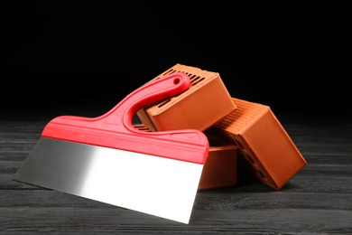 Photo of Red bricks and putty knife on wooden table. Building material