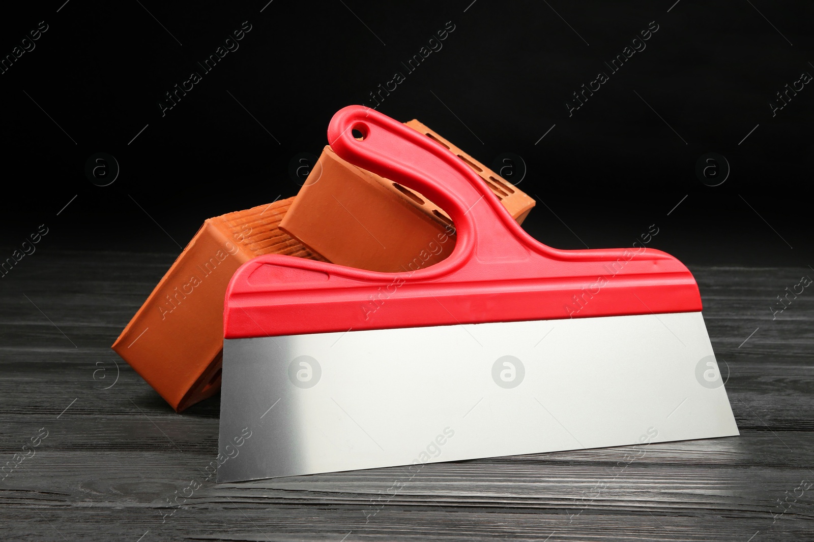 Photo of Red bricks and putty knife on wooden table. Building material