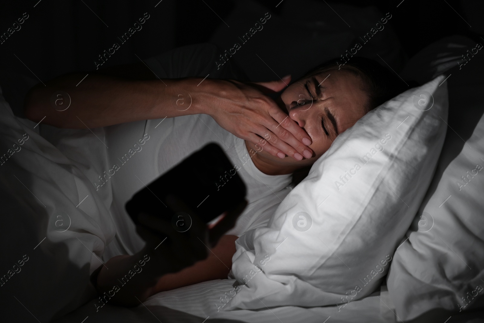 Photo of Bad habit. Young woman using smartphone in bed at night