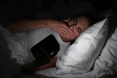 Bad habit. Young woman using smartphone in bed at night