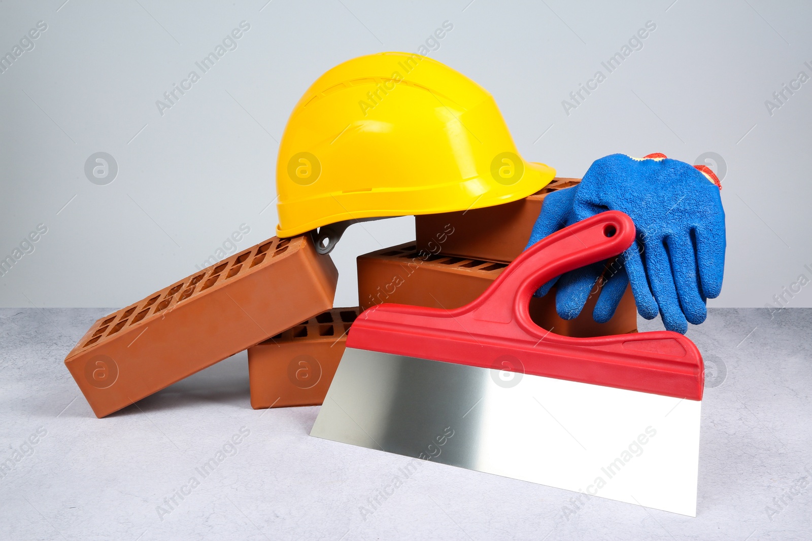 Photo of Red bricks, plastering trowel, gloves and hardhat on textured table against light background