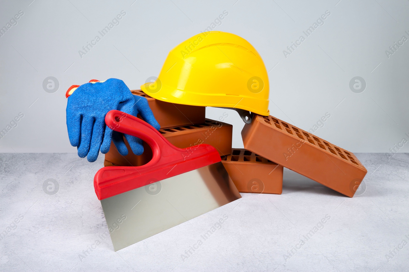 Photo of Red bricks, plastering trowel, gloves and hardhat on textured table against light background