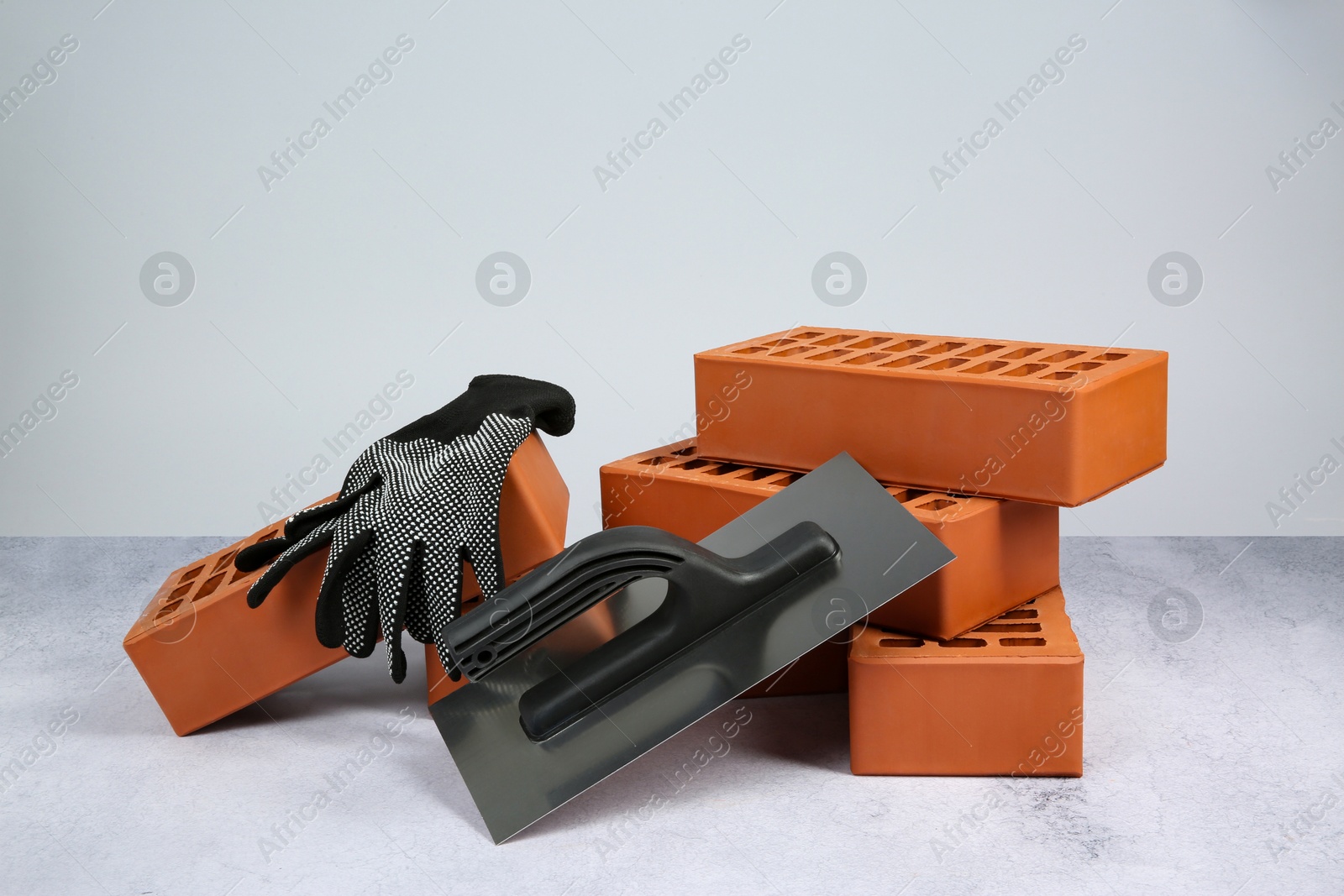 Photo of Red bricks, plastering trowel and gloves on textured table against light background