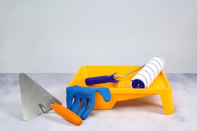 Paint roller, glove, trowel and yellow tray on textured table against light background. Building material