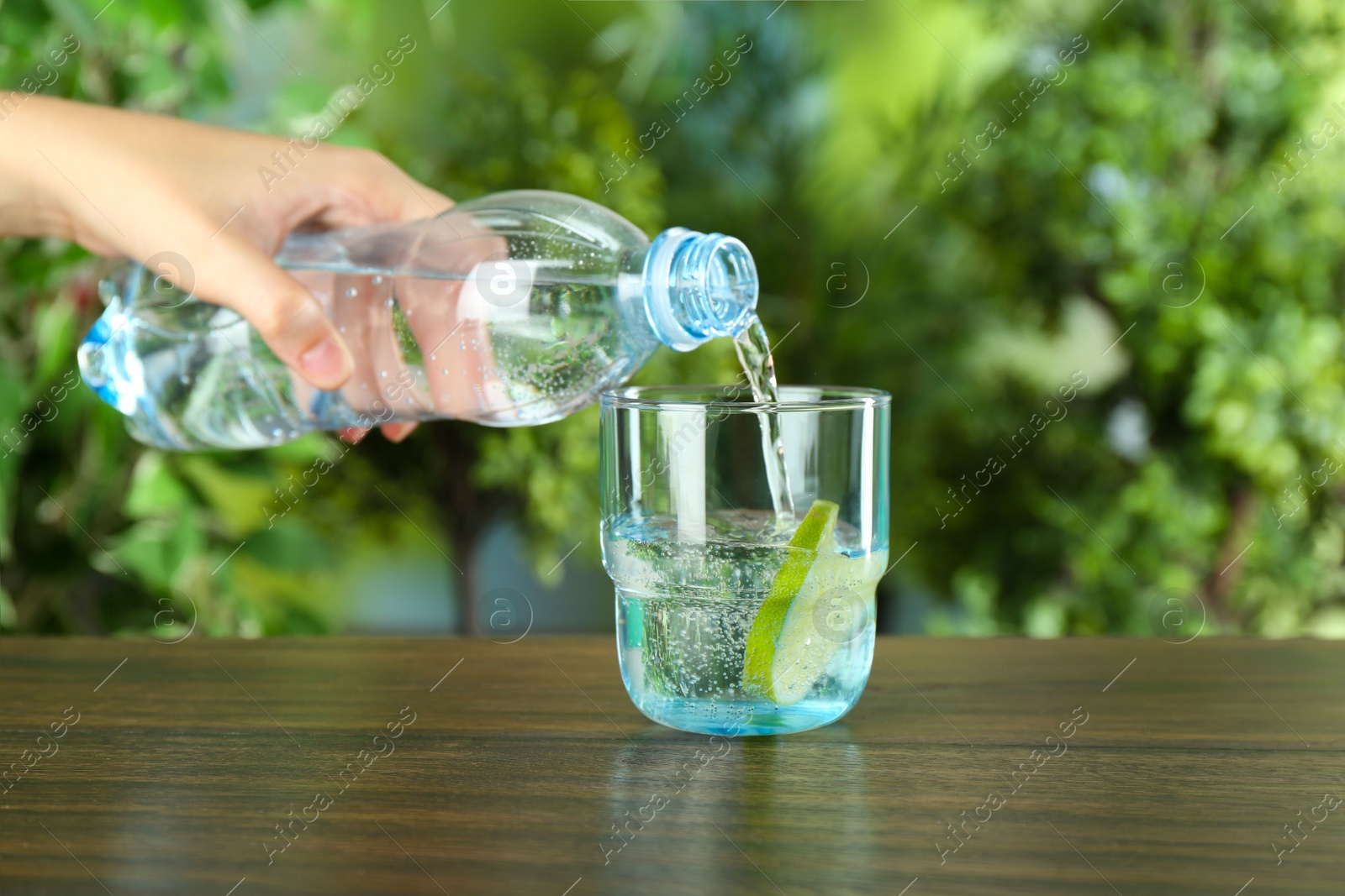 Photo of Woman pouring soda water from bottle into glass at wooden table, closeup