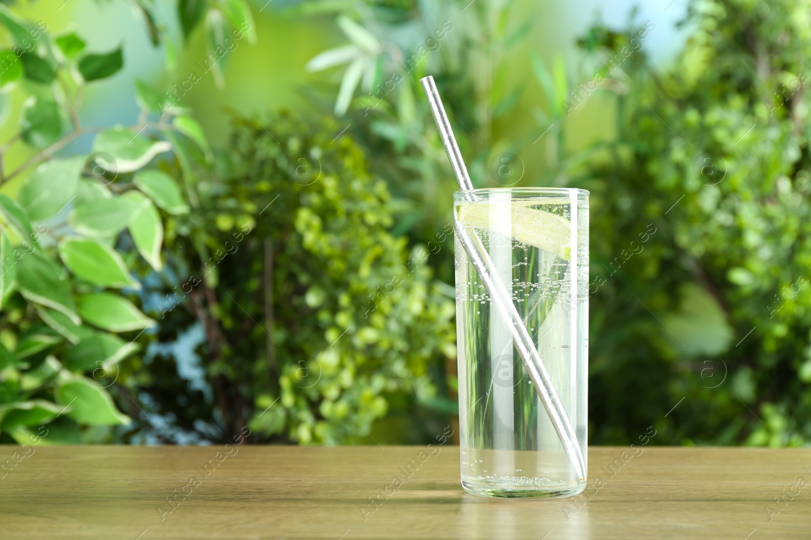 Photo of Glass of soda water with lime on wooden table against blurred background. Space for text