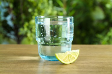 Photo of Glass of soda water with lime on wooden table against blurred background