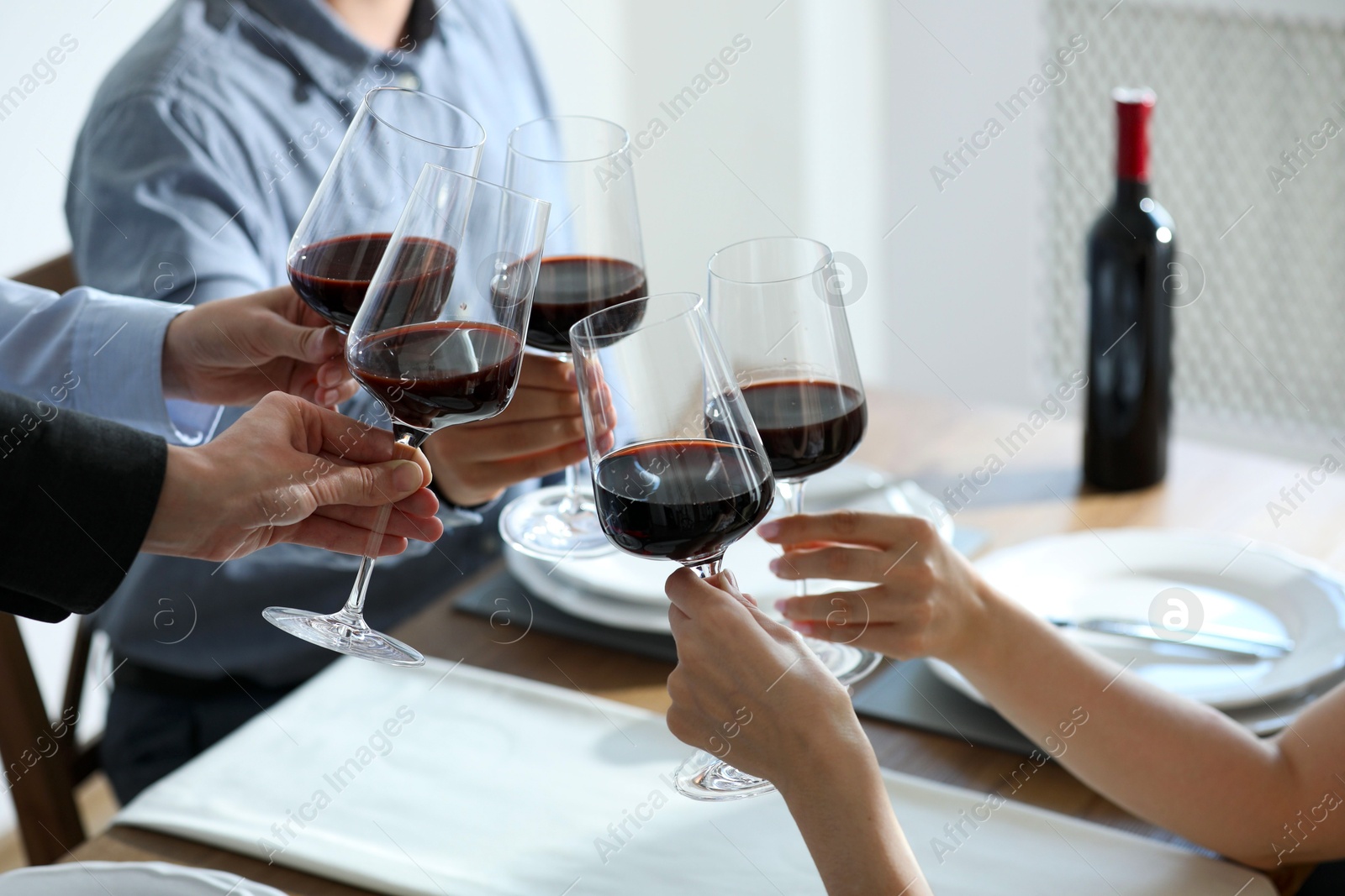 Photo of People clinking glasses of wine indoors, closeup