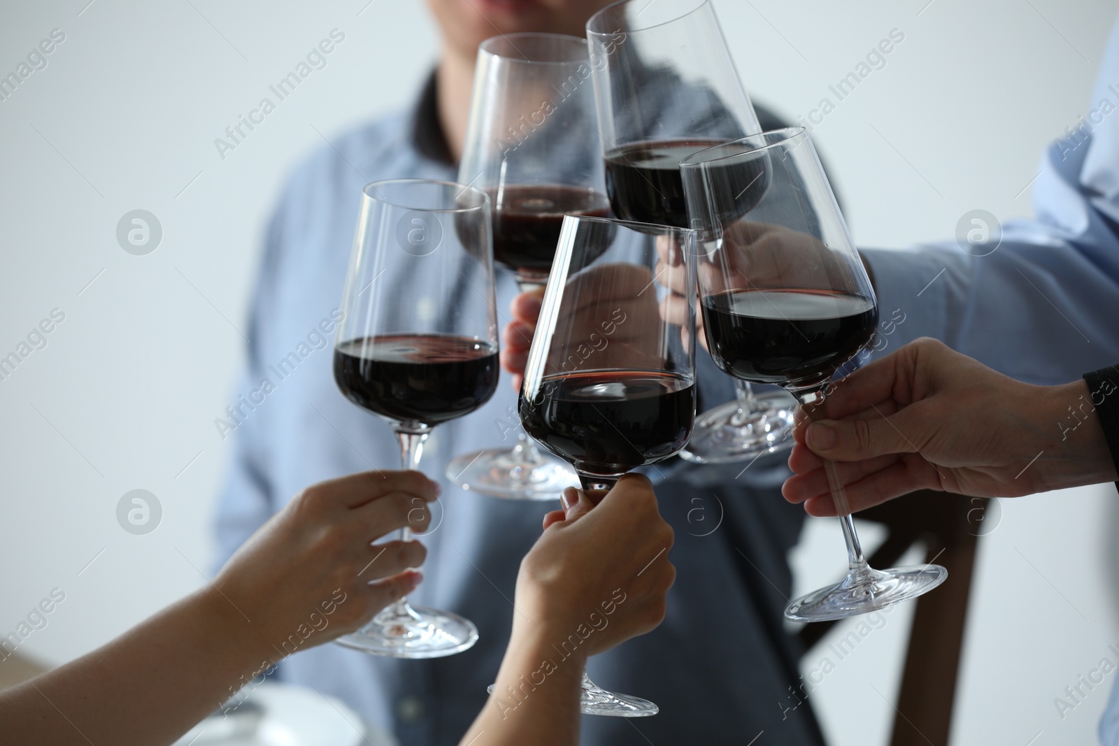 Photo of People clinking glasses of wine indoors, closeup