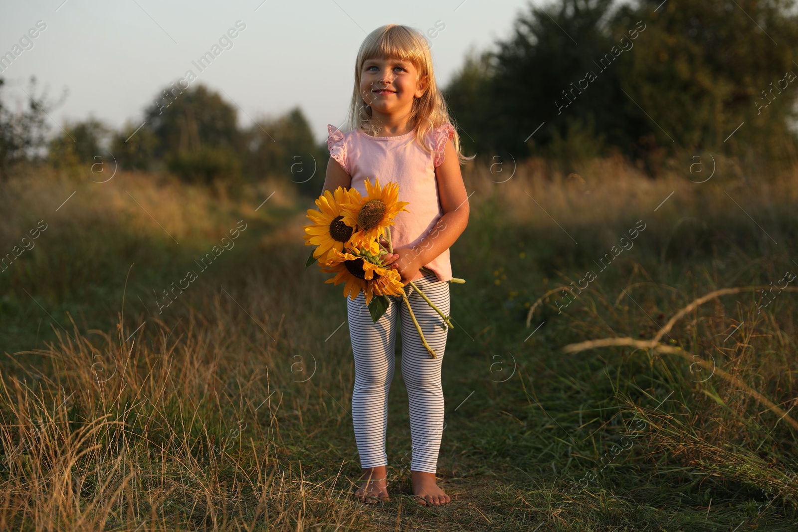 Photo of Little girl with sunflowers at meadow. Child enjoying beautiful nature