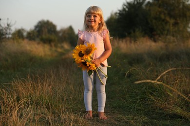 Photo of Little girl with sunflowers at meadow. Child enjoying beautiful nature