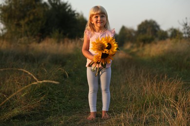 Photo of Little girl with sunflowers at meadow. Child enjoying beautiful nature