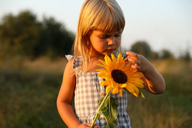 Little girl with sunflower at meadow. Child enjoying beautiful nature