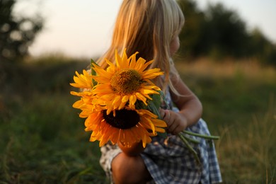 Photo of Little girl with sunflowers at meadow. Child enjoying beautiful nature