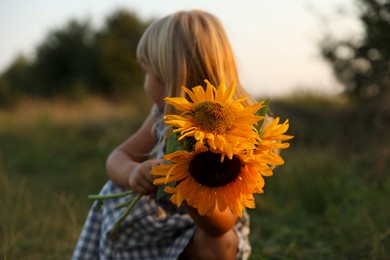 Photo of Little girl with sunflowers at meadow. Child enjoying beautiful nature