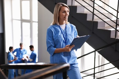 Smiling healthcare worker with clipboard writing notes on stairs in hospital