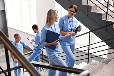 Healthcare workers with tablet and clipboard walking up stairs in hospital