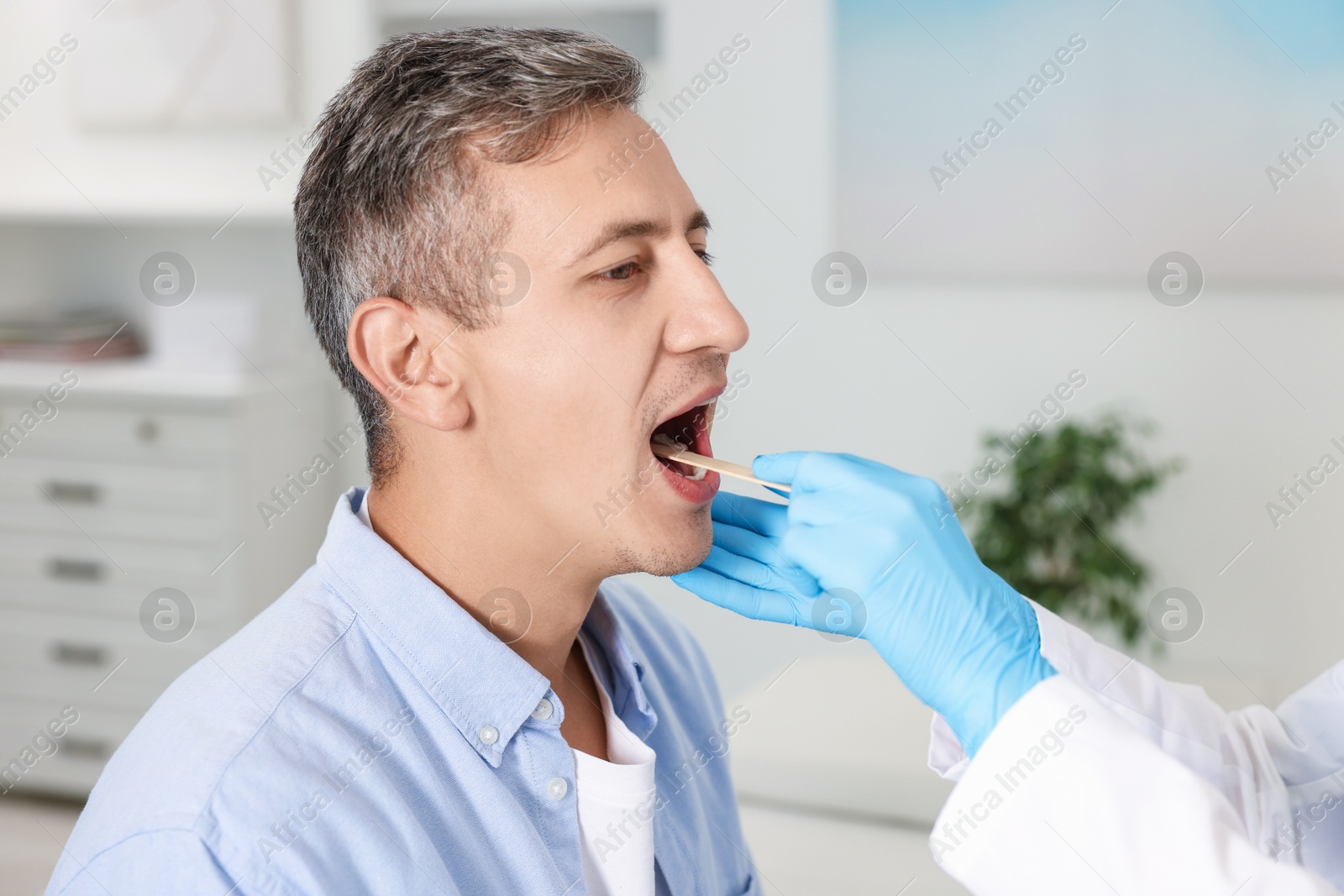 Photo of Doctor examining man's throat with tongue depressor in clinic