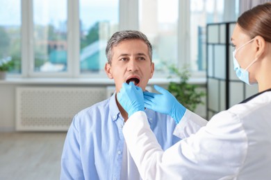 Doctor examining man's throat with tongue depressor in clinic