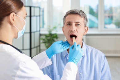 Doctor examining man's throat with tongue depressor in clinic