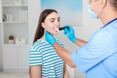 Doctor examining woman's throat with flashlight in clinic