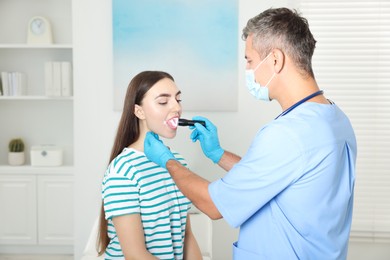 Doctor examining woman's throat with flashlight in clinic