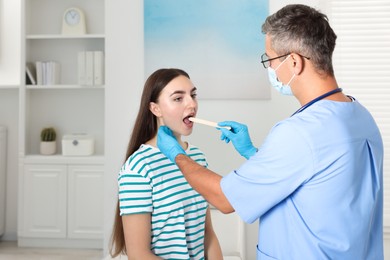 Doctor examining woman's throat with tongue depressor in clinic