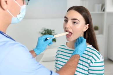 Doctor examining woman's throat with tongue depressor in clinic