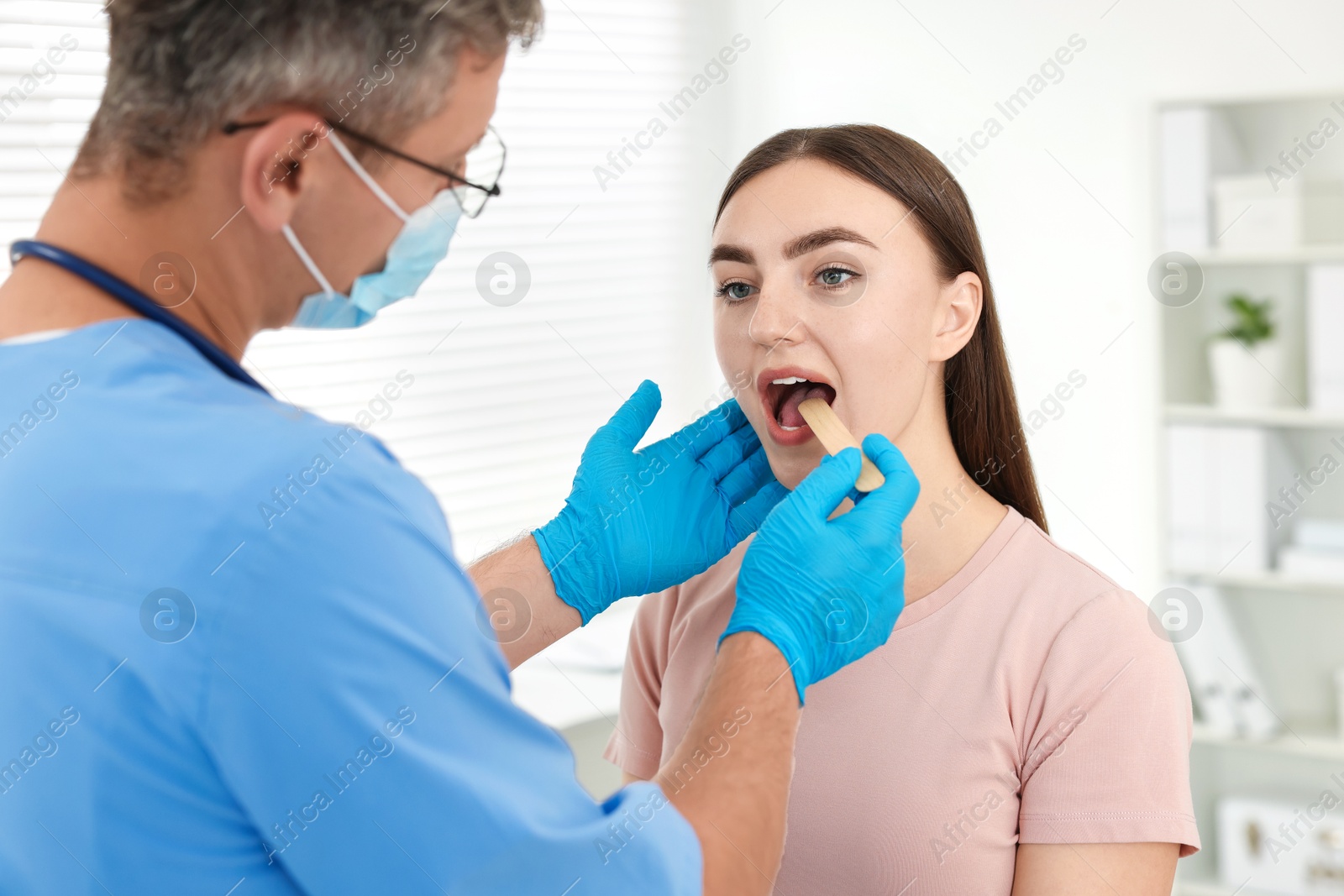 Photo of Doctor examining woman's throat with tongue depressor in clinic