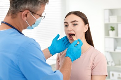 Doctor examining woman's throat with tongue depressor in clinic