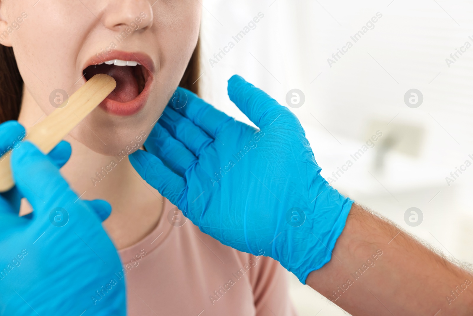 Photo of Doctor examining woman's throat with tongue depressor in clinic, closeup