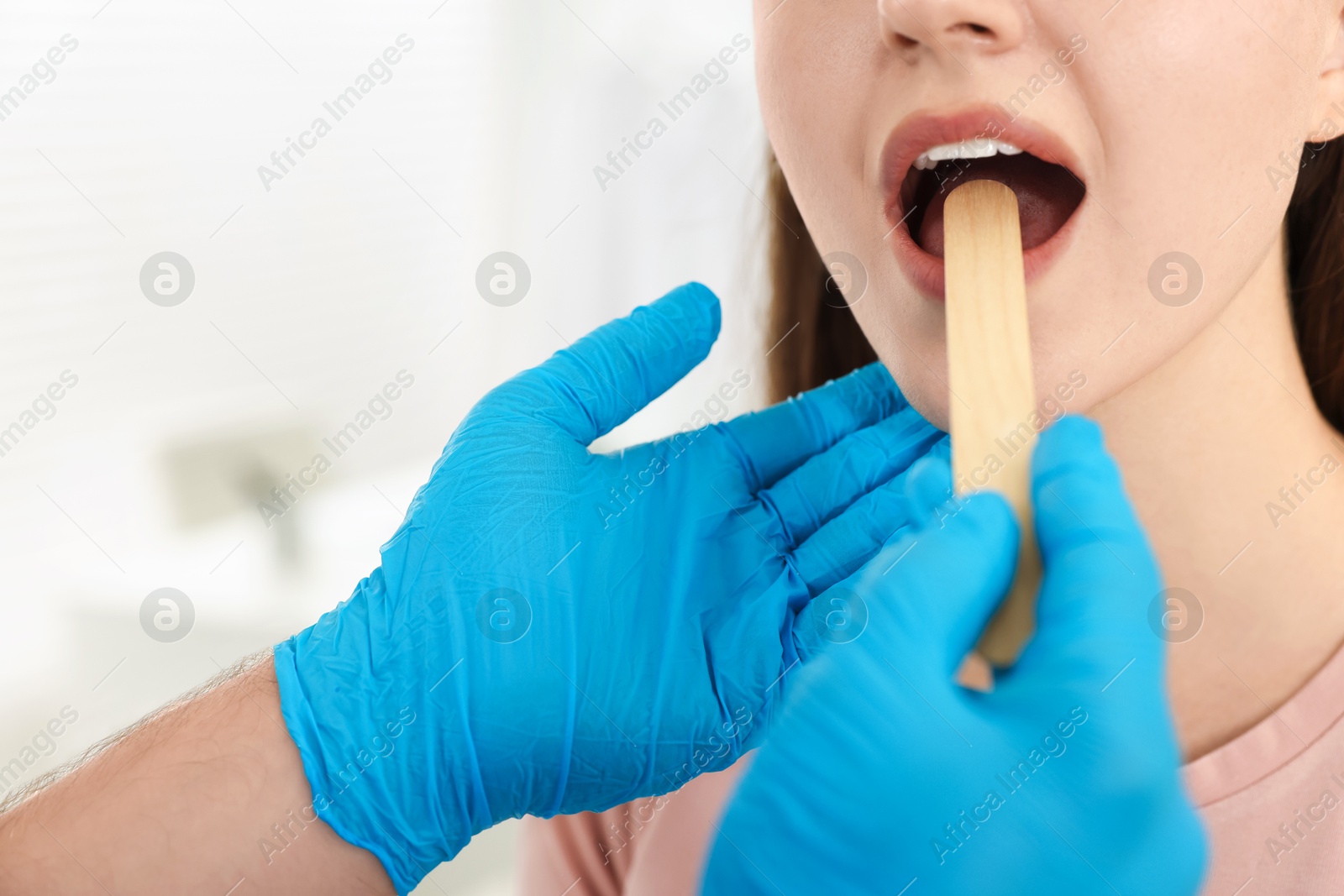 Photo of Doctor examining woman's throat with tongue depressor in clinic, closeup