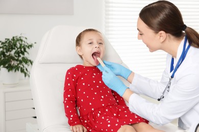 Doctor examining girl's throat with tongue depressor in clinic