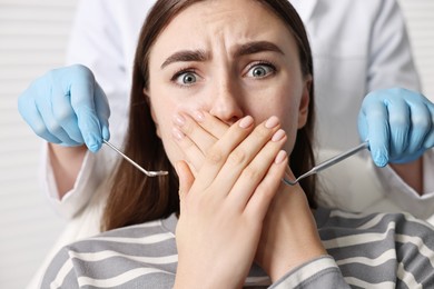 Photo of Dental phobia. Dentist working with scared woman in clinic, closeup