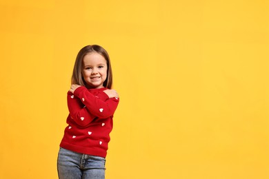 Photo of Cute little girl hugging herself on yellow background, space for text