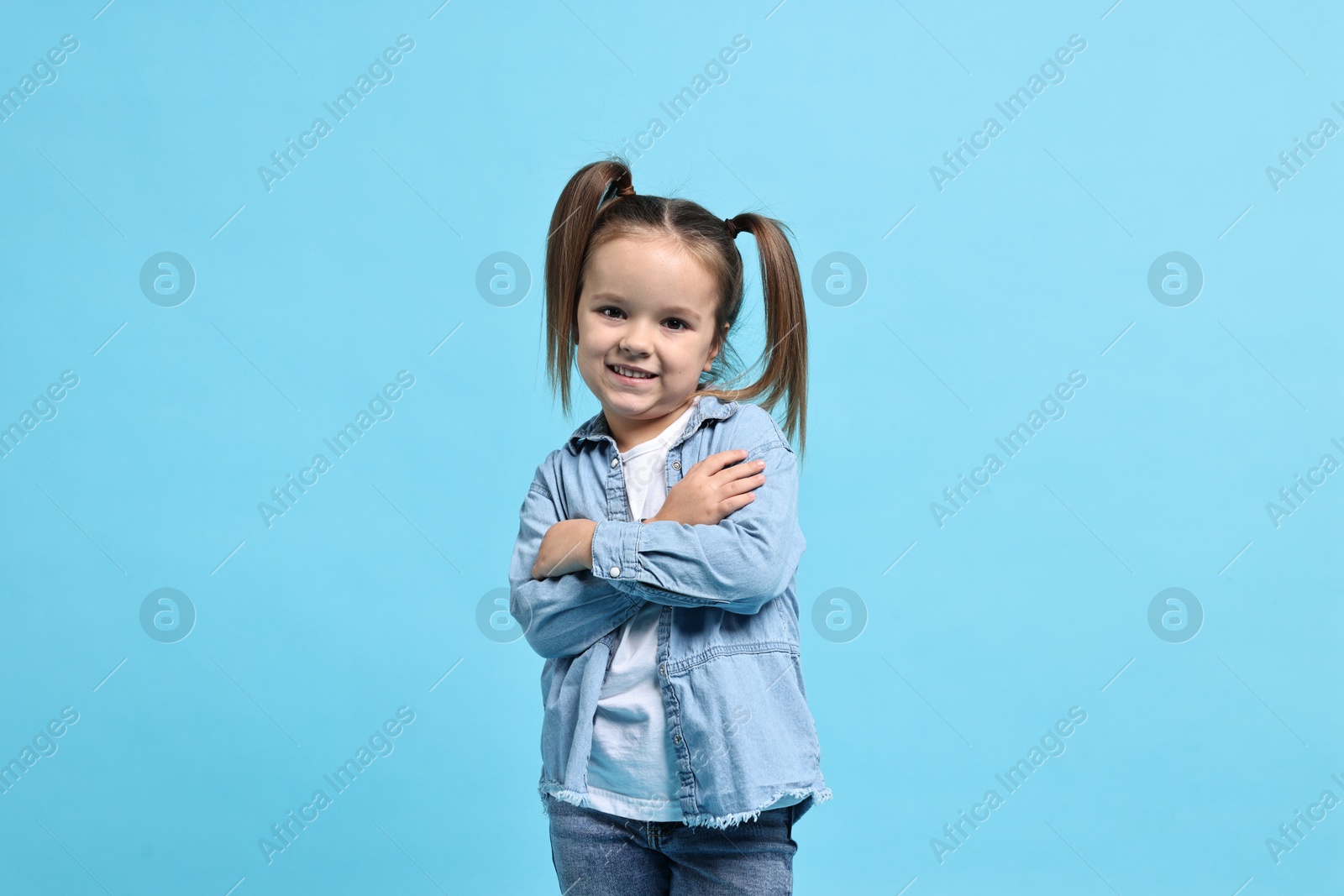 Photo of Cute little girl hugging herself on light blue background