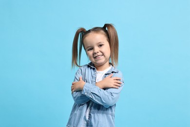 Photo of Cute little girl hugging herself on light blue background