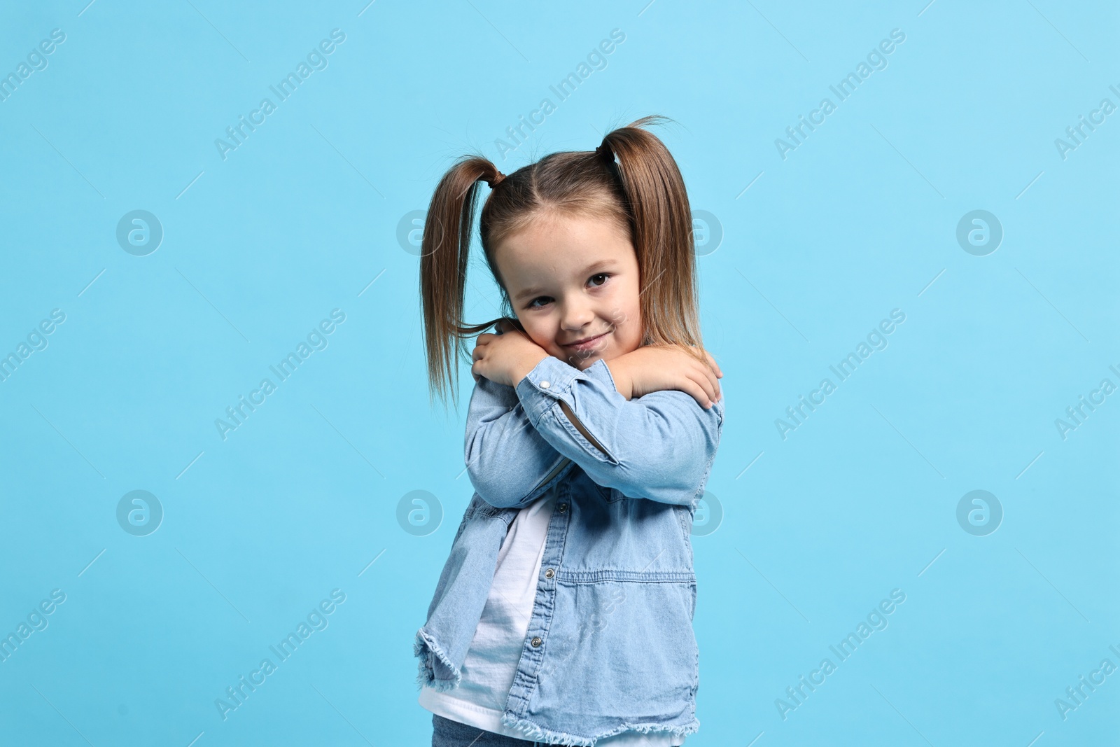 Photo of Cute little girl hugging herself on light blue background