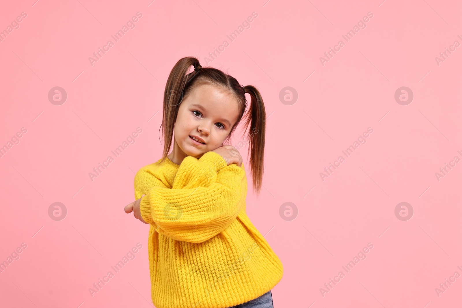 Photo of Cute little girl hugging herself on pink background, space for text