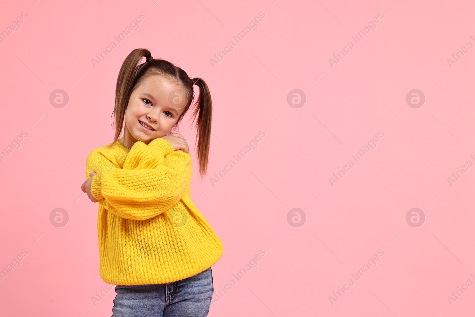 Photo of Cute little girl hugging herself on pink background, space for text