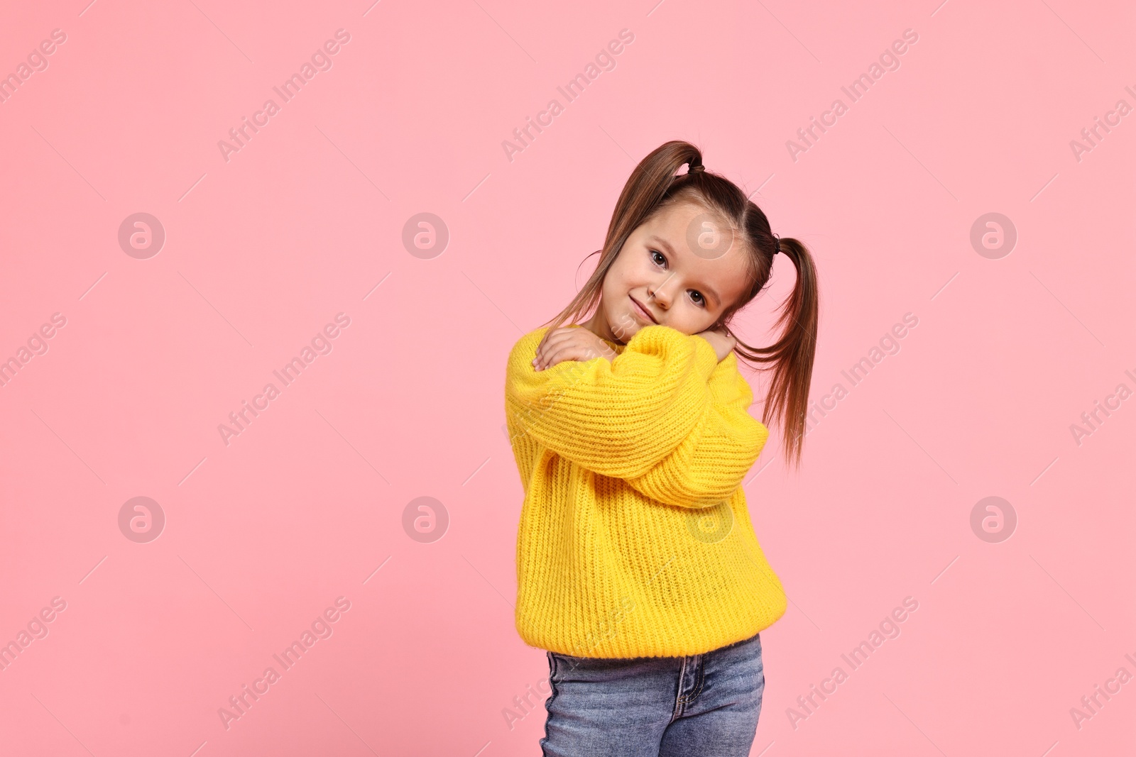 Photo of Cute little girl hugging herself on pink background, space for text