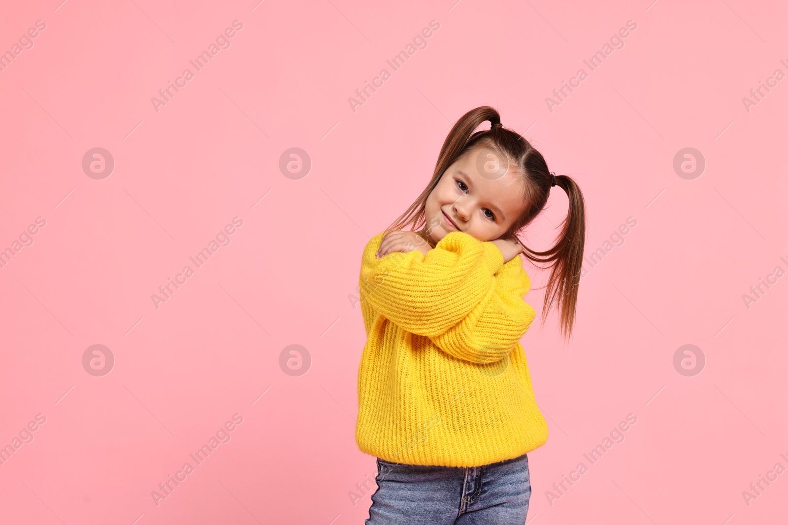 Photo of Cute little girl hugging herself on pink background, space for text