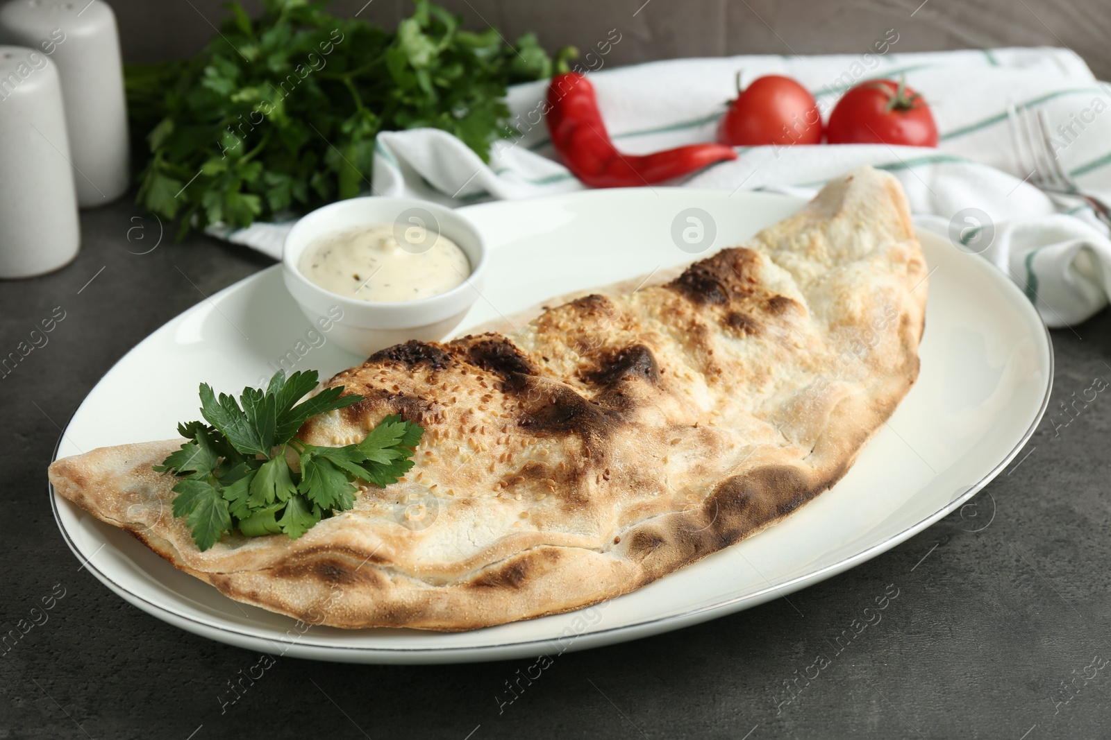 Photo of Delicious calzone served with sauce on grey table, closeup