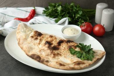 Photo of Delicious calzone served with sauce on grey table, closeup