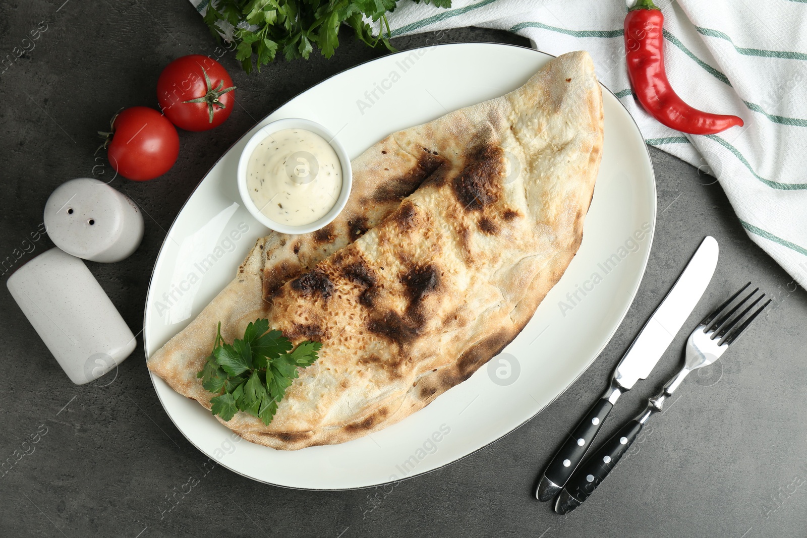 Photo of Delicious calzone served with sauce on grey table, flat lay